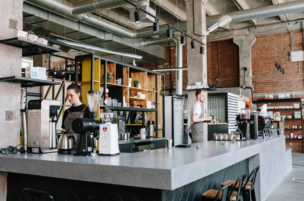 Baristas working in a trendy industrial-style coffee shop with exposed brick and beams.